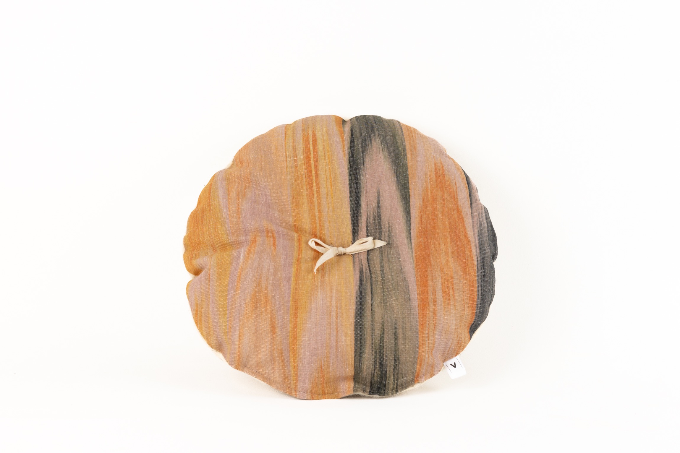 Cojín redondo con estampado ikat en tonos tierra y lazo decorativo en el centro